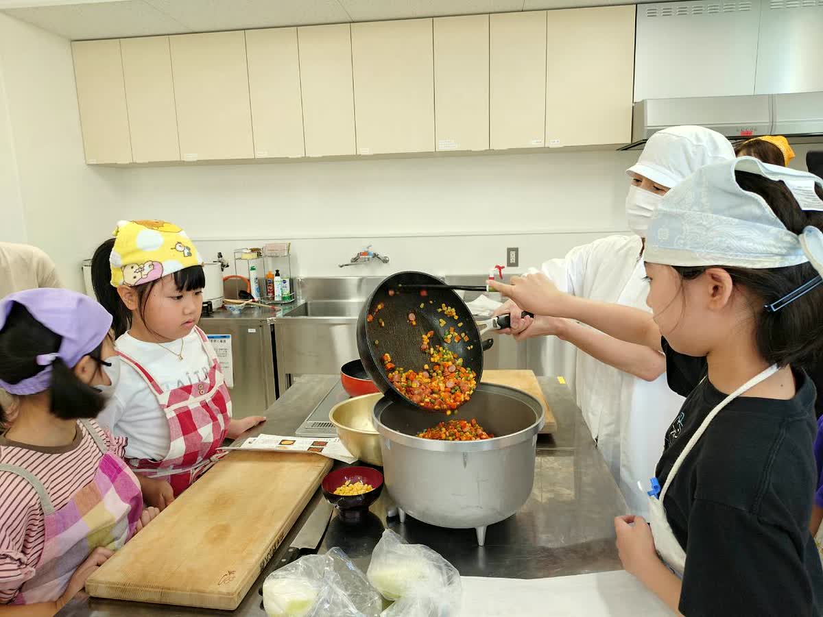 北日野自治振興会 炒めた具材を炊飯器に入れる子どもたち
