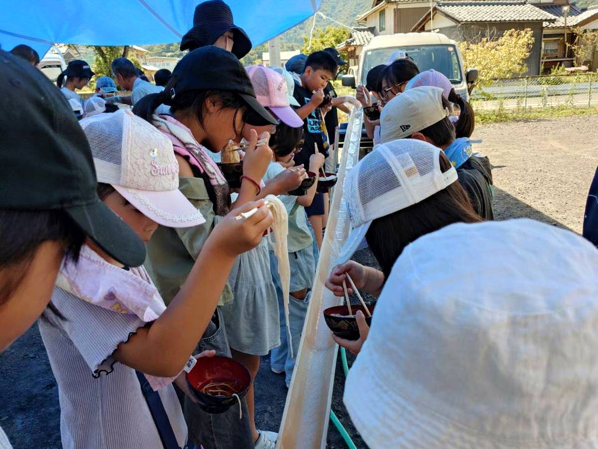 北日野自治振興会 長い竹台の両側で流しそうめんを楽しむ様子