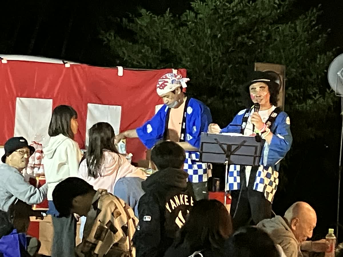 北日野自治振興会 帆山町秋祭りの福引きで司会をする会長と集まった町民